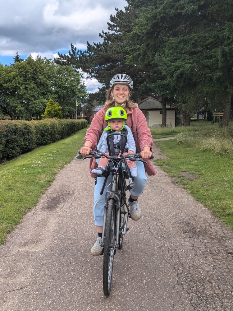 Cycling while breastfeeding: a woman seen from the front, cycling with a baby in a front-mounted child seat