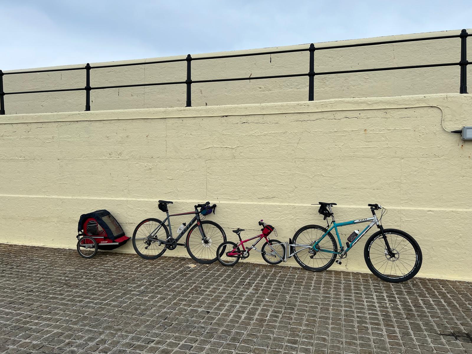Family bike ride with the FollowMe Tandem reivew. 2 adult bikes, a childs bike and a trailer leant against a watt