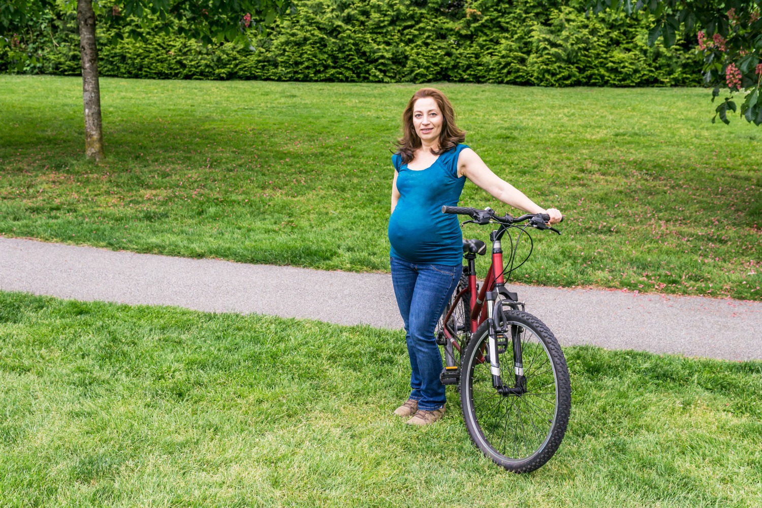 pregnant woman standing next to her red bike