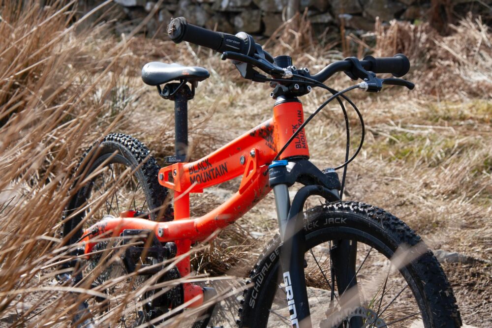 Black Mountain HÜTTO 20″ review- a photo of the orange child's mountain bike in a grassy field