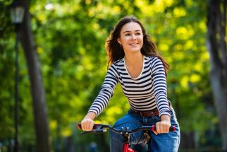 A teenage girl riding a bike past some trees and smiling