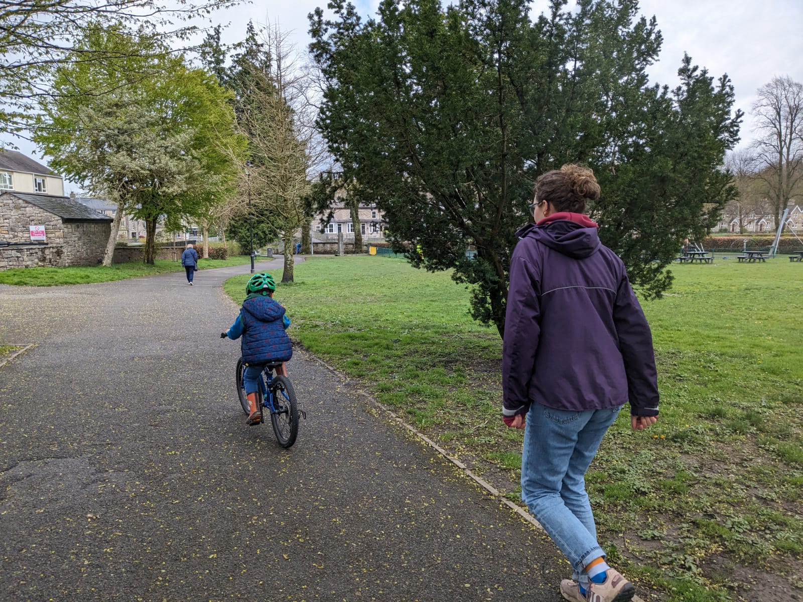 little boy learning to ride a bike and an adult in a purple jacket is running along behind