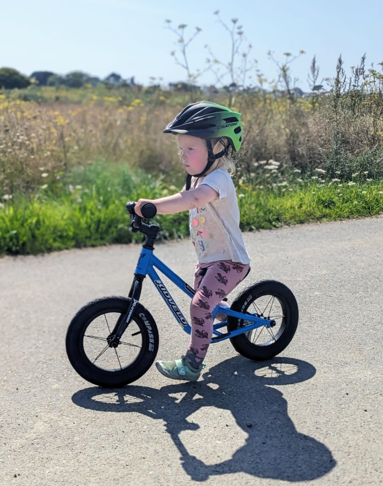 Kidvelo Rookie 12 review: little girl riding on a sunny day on a blue balance bike