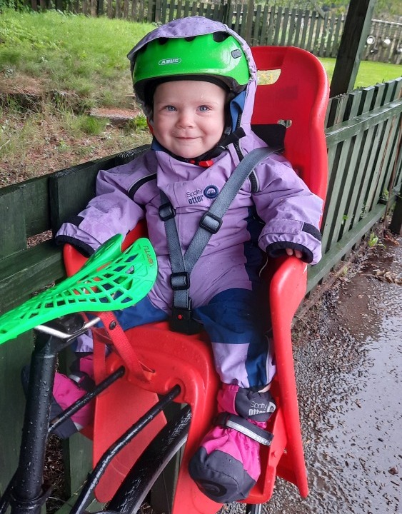 first family bike ride: A baby in a rear bike seat, wearing a brightly coloured helmet, and smiling