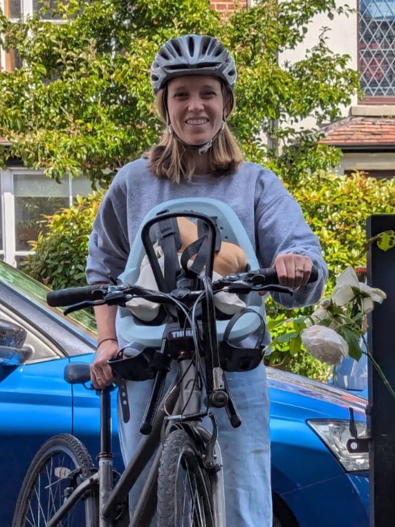 first family bike ride: A mum wheeling her bike in from the street, with the front seat filled with vegetables