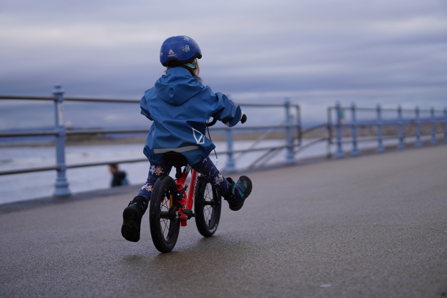 a girl in a blue coat happily gliding on her kidvelo rookie 14 balance bike by the seaside