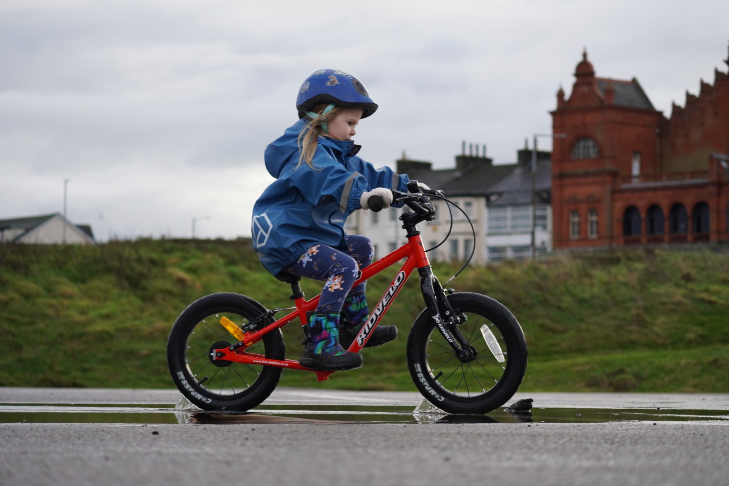 a girl in a blue coat happily gliding on her kidvelo rookie 14 balance bike by the seaside