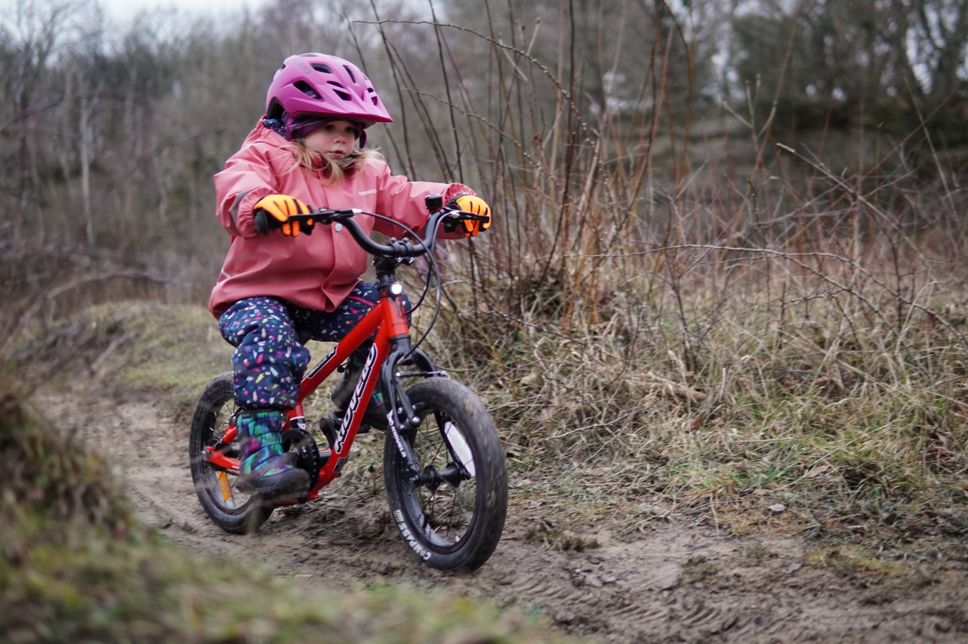 a girl in a pink coat happily gliding on her kidvelo rookie 14 balance bike by the seaside