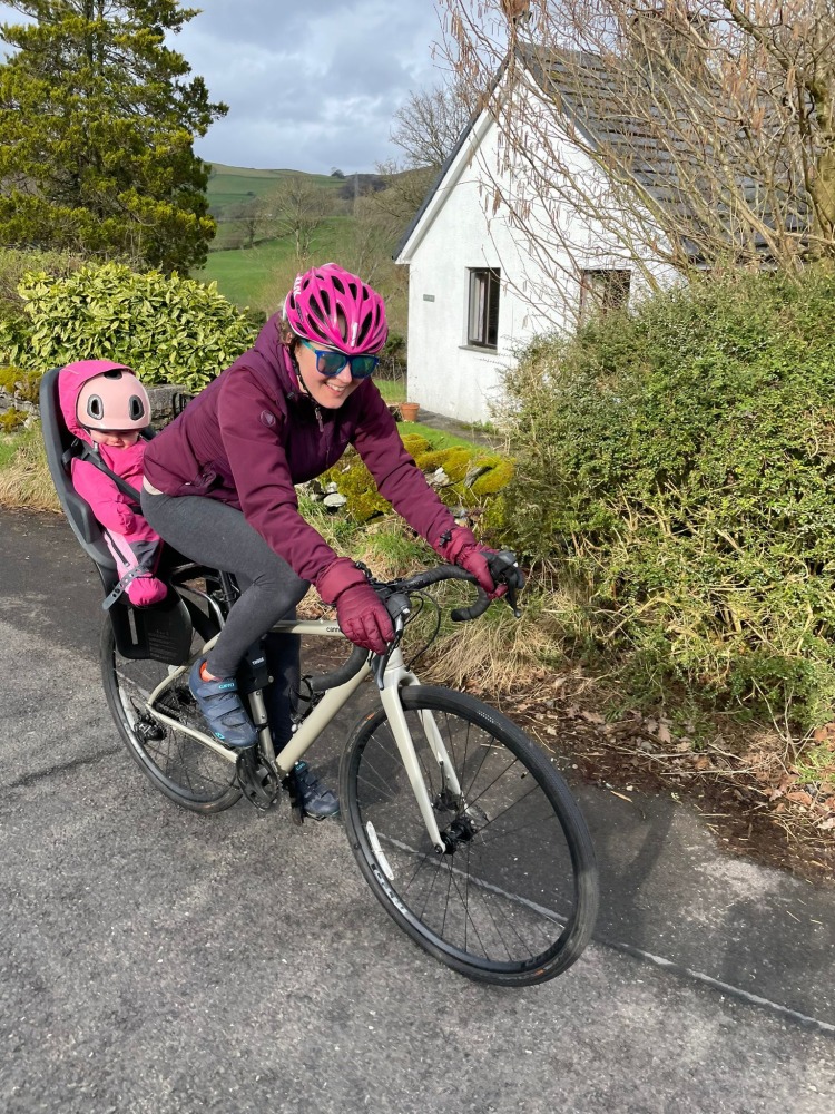 Thule Yepp 2 Maxi rear seat in use, a little girl in a pink onesie on the back of her parents bike