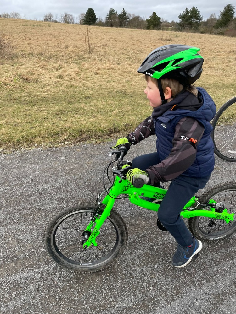 boy in a TI-GO BMX Hoodie riding a green bike on a gravel trail