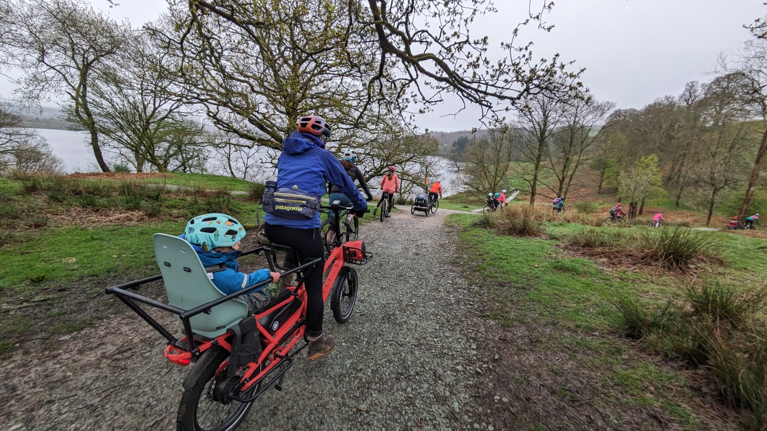 woman riding the Estarli ecargo longtail bike with her toddler on the back next to a lake