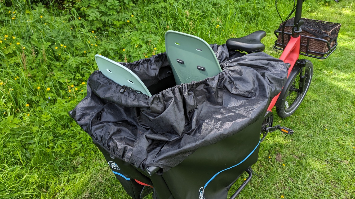 Estarli ecargo longtail bike with two rear child seats and rain cover agains a grassy background