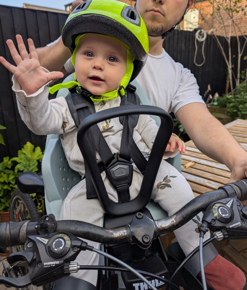 Thule Yepp 2 mini review:a little girl in a yellow helmet sat in a Thule Yepp 2 Mini front bike seat is waving at the camera