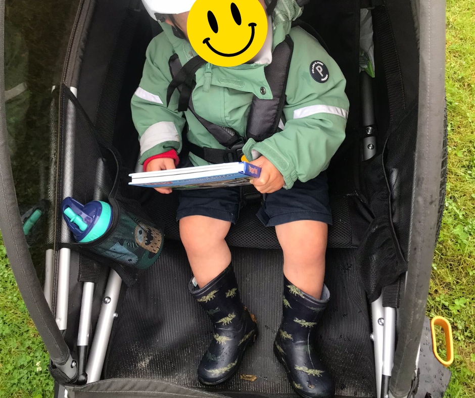 a little boy sitting in a burley D'Lite X trailer reading a book