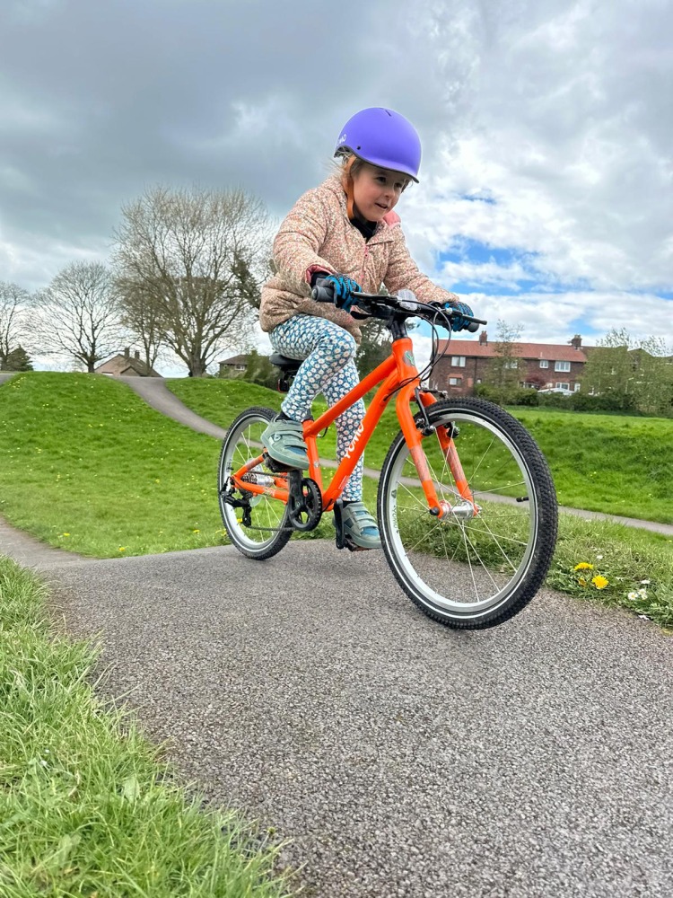 A young girl riding an orange Yomo 20 on a pump track