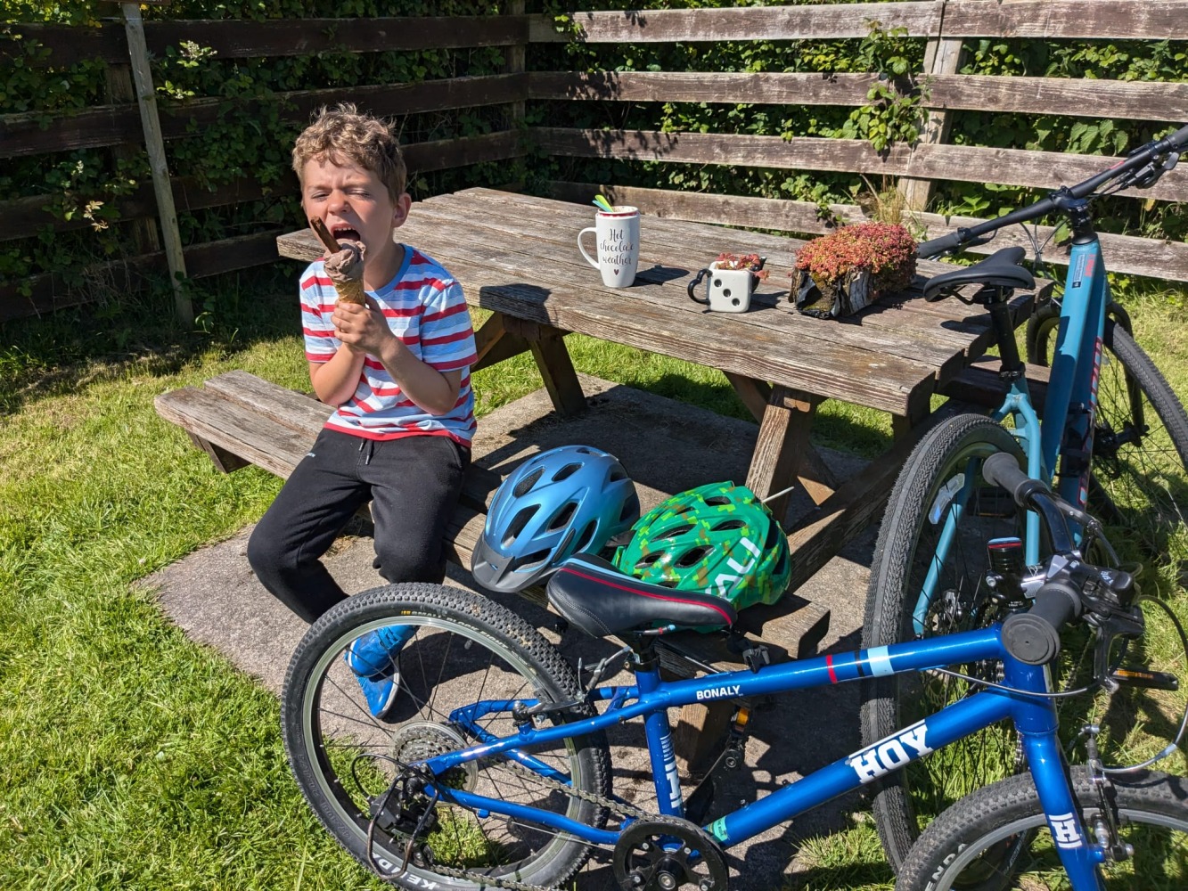 a boy eating an ice cream sat on a bench next to his bike