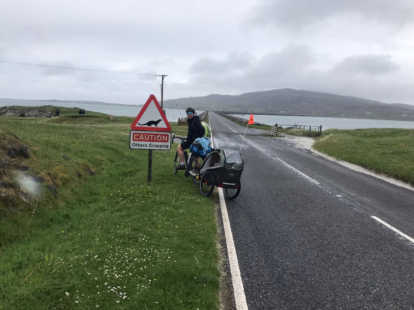 dad riding with the Burley D'Lite X child trailer in scotland with an 'otter crossing' sign behind him.