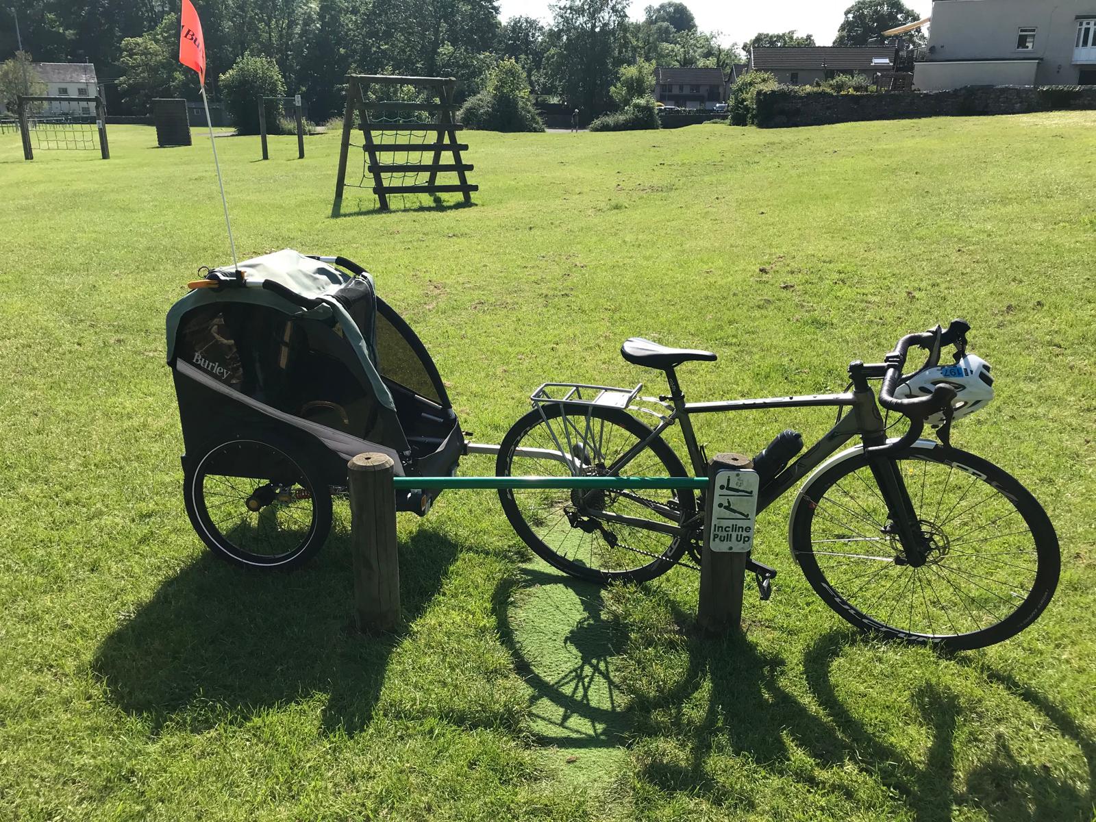 Burley D'Lite X child trailer hitched to an adult bike leaning against a spot on a grassy field