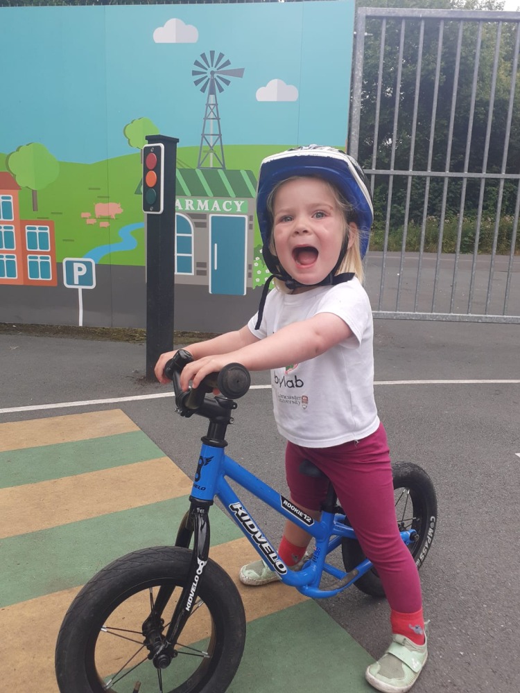 Kidvelo Rookie 12 review: little girl riding a blue balance bike on a pretend zebra crossing in a play park