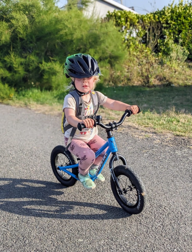 Kidvelo Rookie 12 review: little girl riding on a sunny day on a blue balance bike