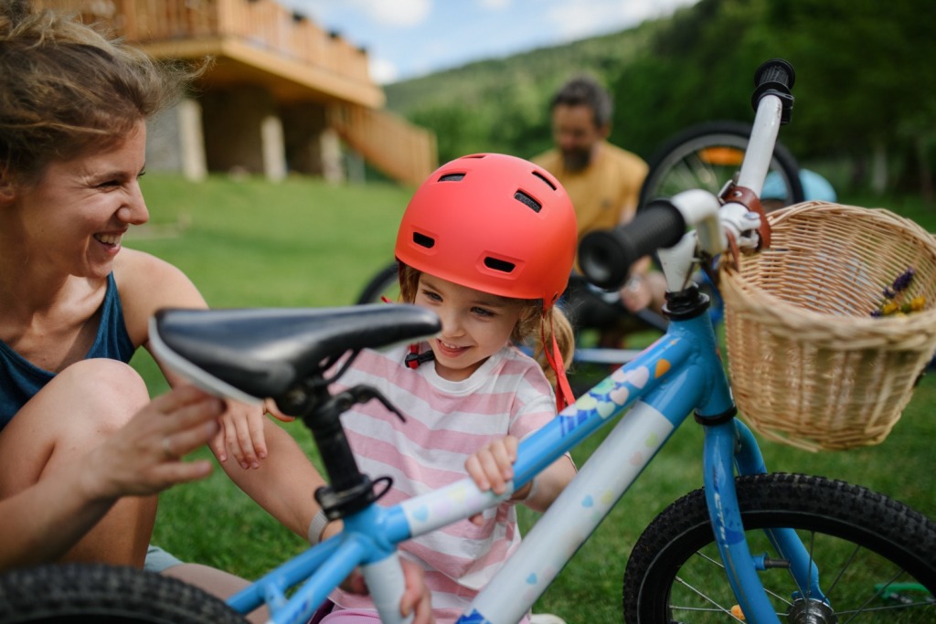 kids bike saddles: little girl wearing a pink helmet is adjusting the saddle height on her bike