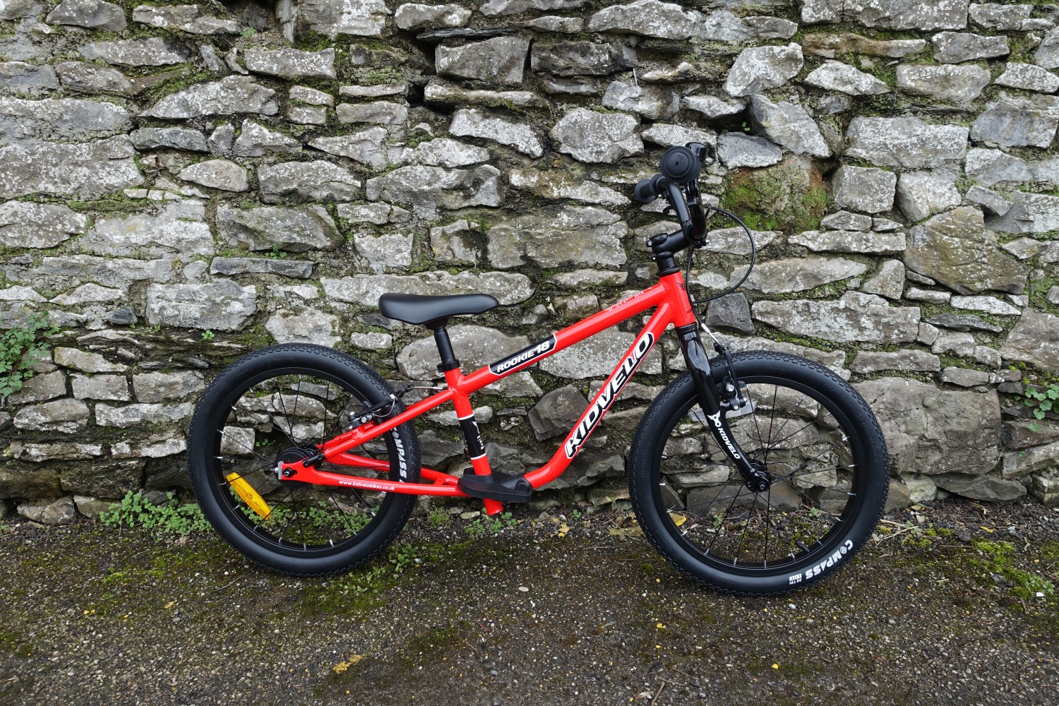 The kidvelo rookie 18 bike in red leant against a wall