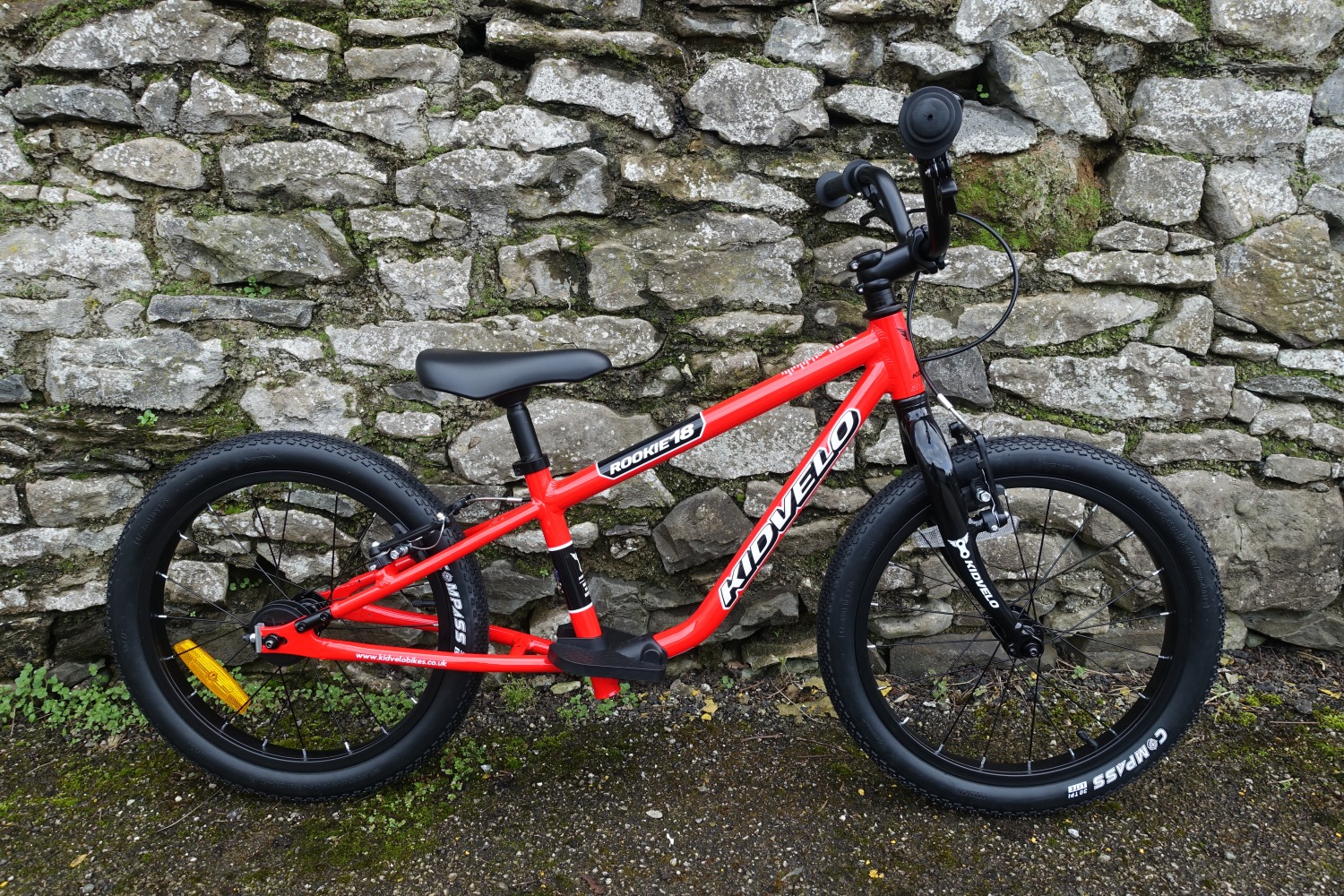 The kidvelo rookie 18 bike in red leant against a wall