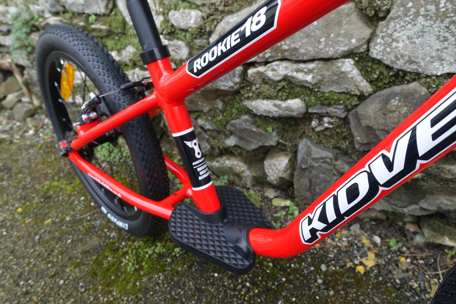 The kidvelo rookie 18 bike in red leant against a wall- a close up of the foot rest