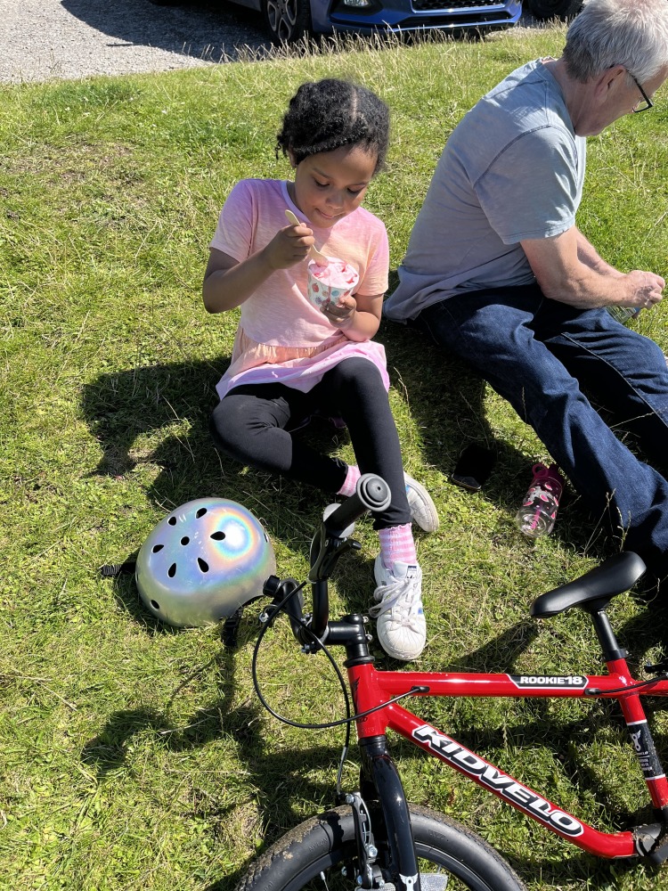 A black girl in a pink top eating ice cream mid ride on her kidvelo rookie 18