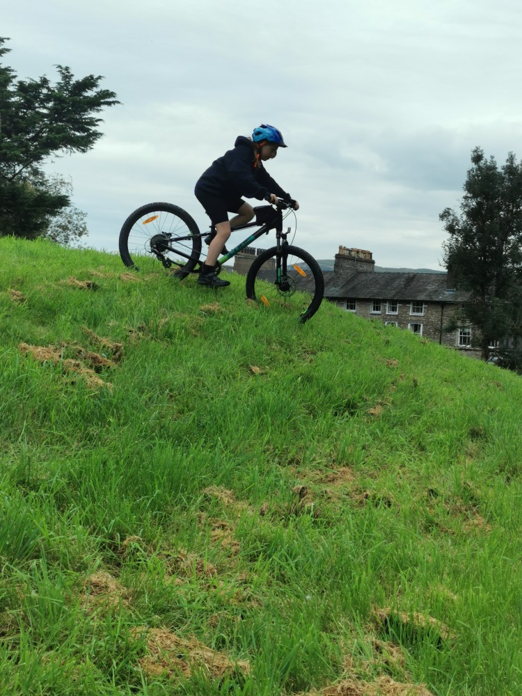 Cube acid 240 MTB review- a girl in a navy hoodie is riding the cube acid mtb down a grassy slope