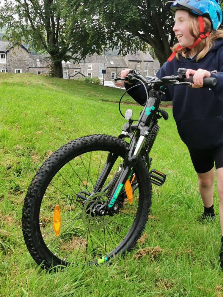 Cube acid 240 MTB review- a girl in a navy hoodie is pushing the cube acid mtb up a grassy slope