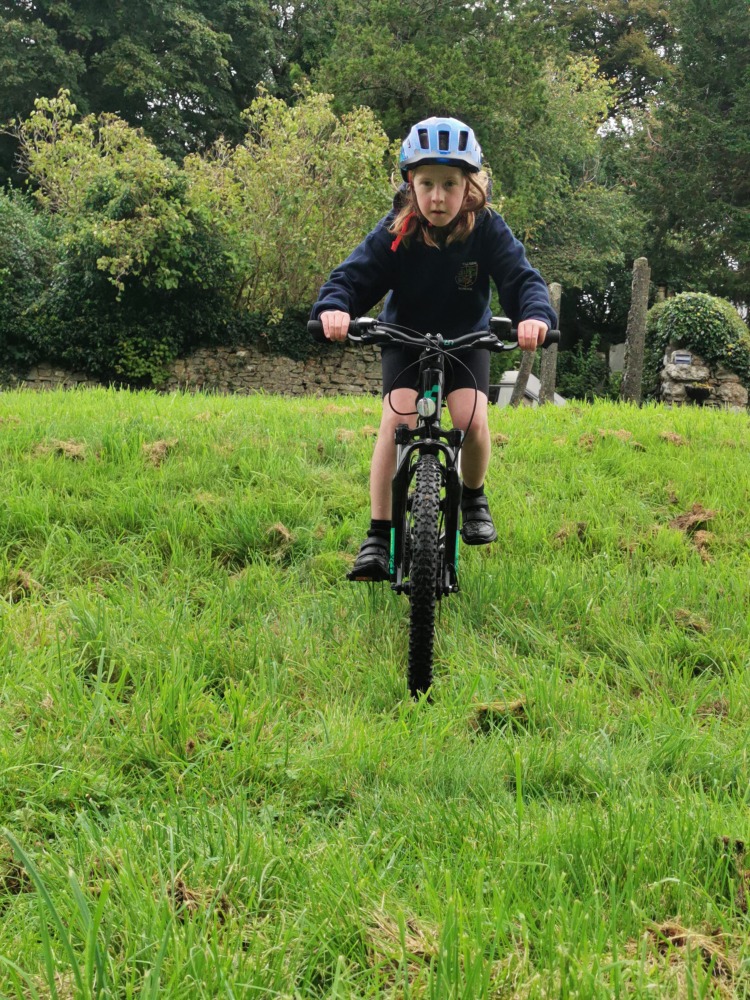 Cube acid 240 MTB review- a girl in a navy hoodie is riding the cube acid mtb down a grassy slope