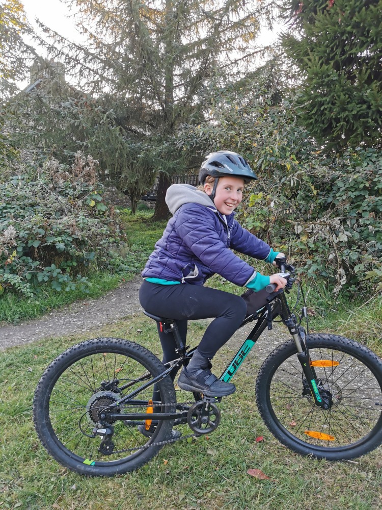 Cube acid 240 MTB review- a girl in a navy hoodie is riding the cube acid mtb down a grassy slope