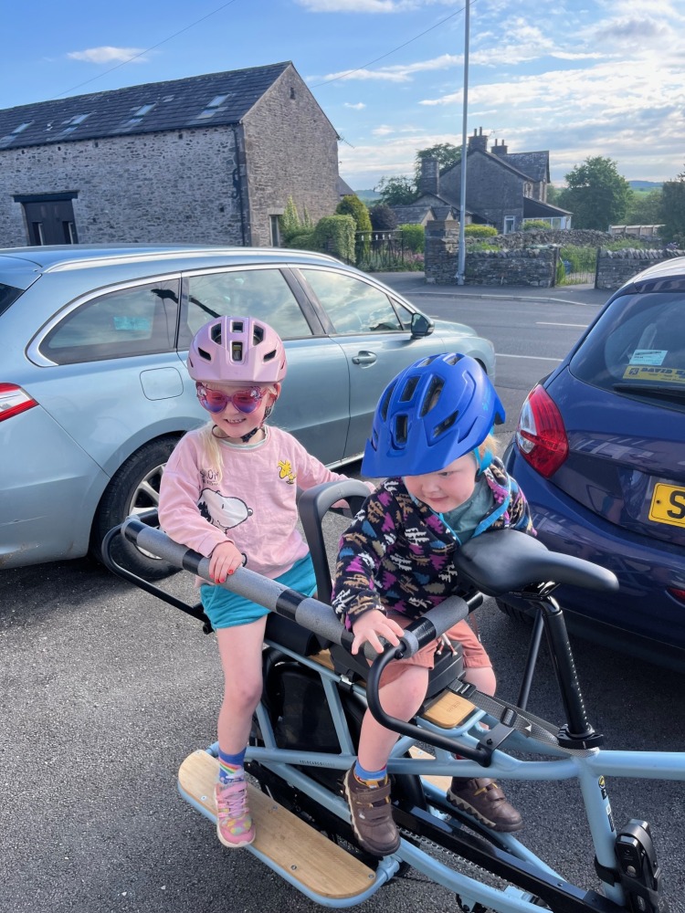 two children in colourful clothes are on the back of their decathlon longtail cargo bike ready to cycle