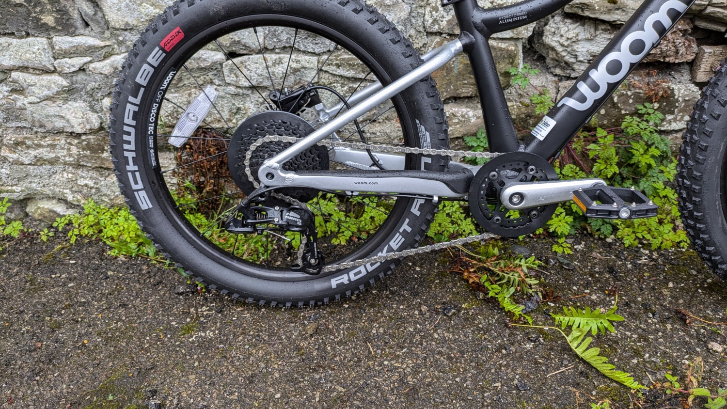 A black and silver woom OFF 4 leant against a stone wall- a close up of the drivetrain