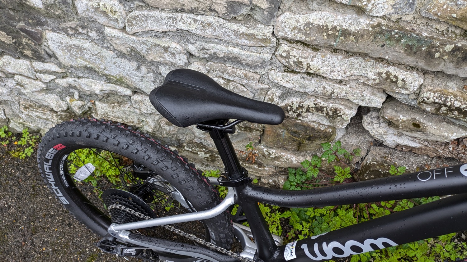 A black and silver woom OFF 4 leant against a stone wall- a close up of the pedal and saddle