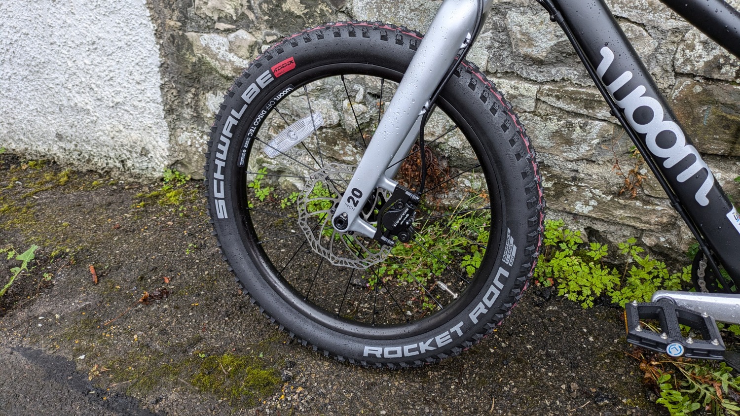 A black and silver woom OFF 4 leant against a stone wall- a close up of the front brake