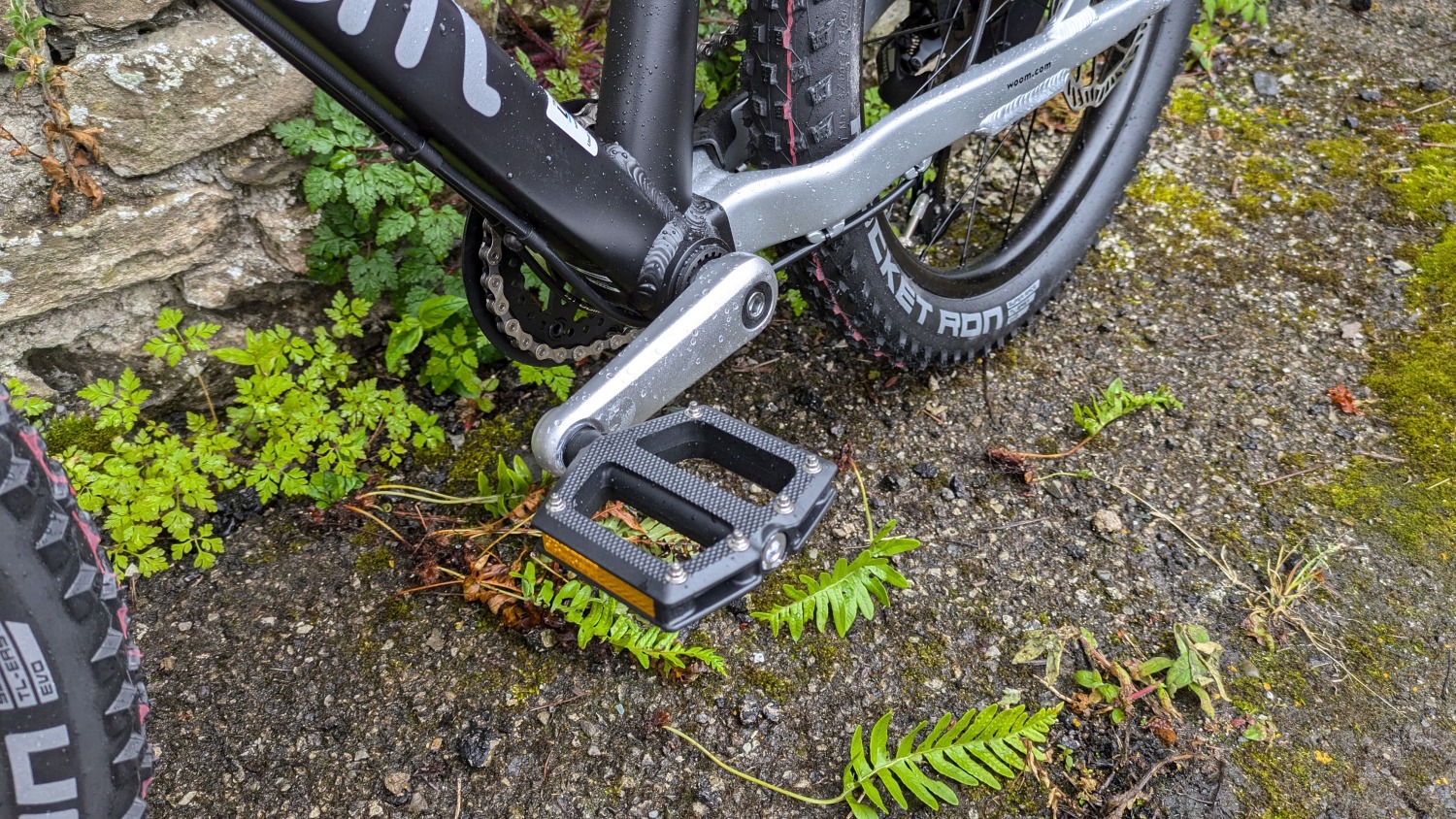 A black and silver woom OFF 4 leant against a stone wall- a close up of the pedal and crank