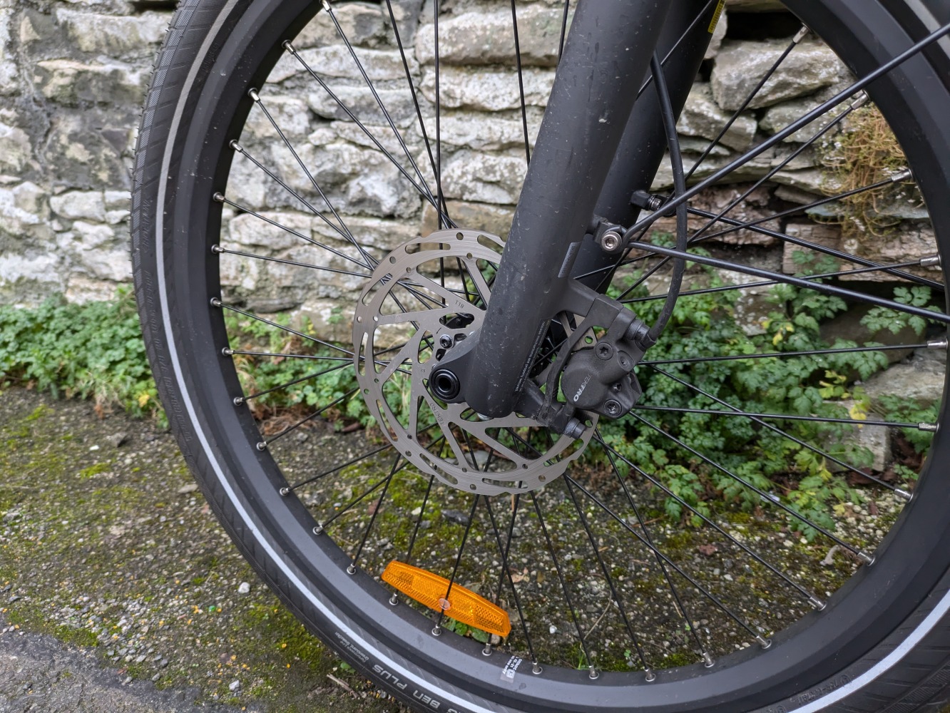 photo of the front brake rotor of a light blue Decathlon longtail cargo bike with a rear rain cover on leant against a brick wall