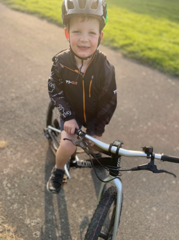 our woom off 4 reviewer Zack riding his bike on a sunny evening while wearing a green helmet and TIGO hoodie