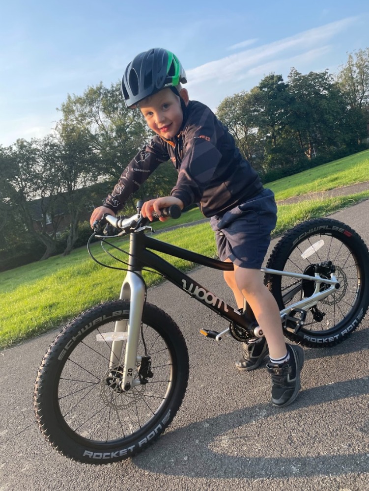 our woom off 4 reviewer Zack riding his bike on a sunny evening while wearing a green helmet and TIGO hoodie