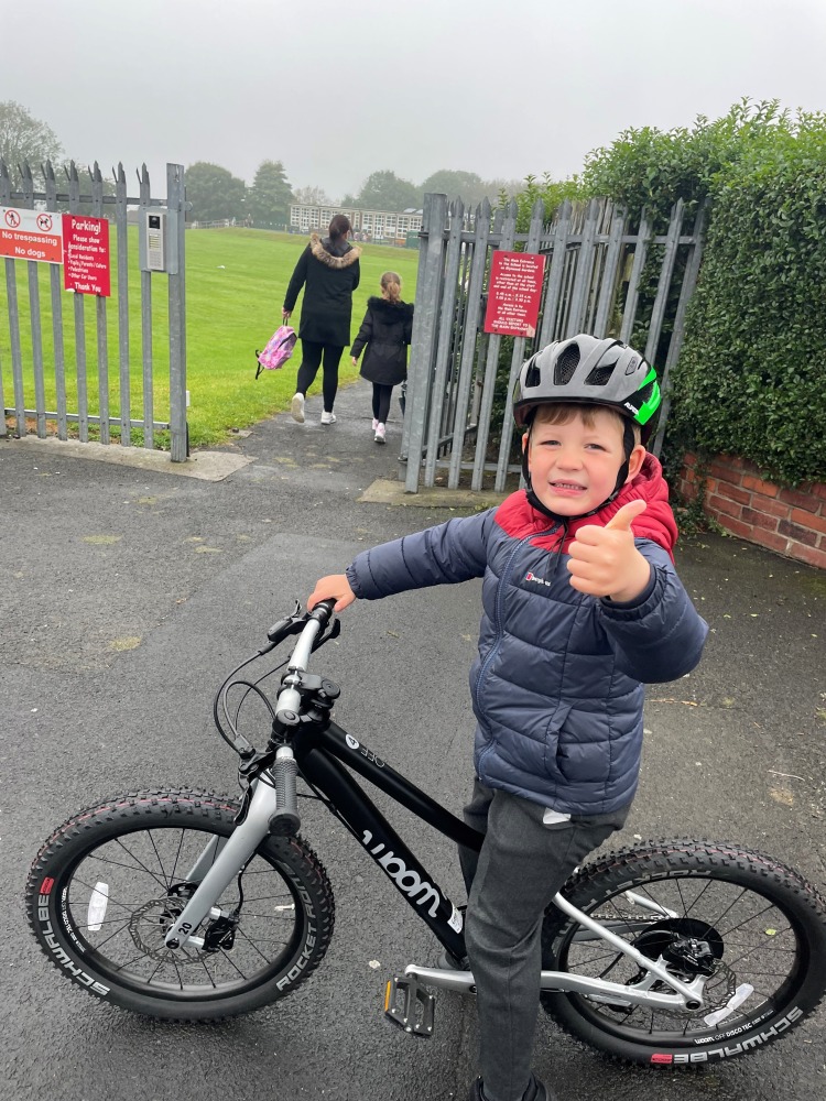 our woom off 4 reviewer Zack riding his bike while wearing a green helmet and a warm blue jacket outside his school