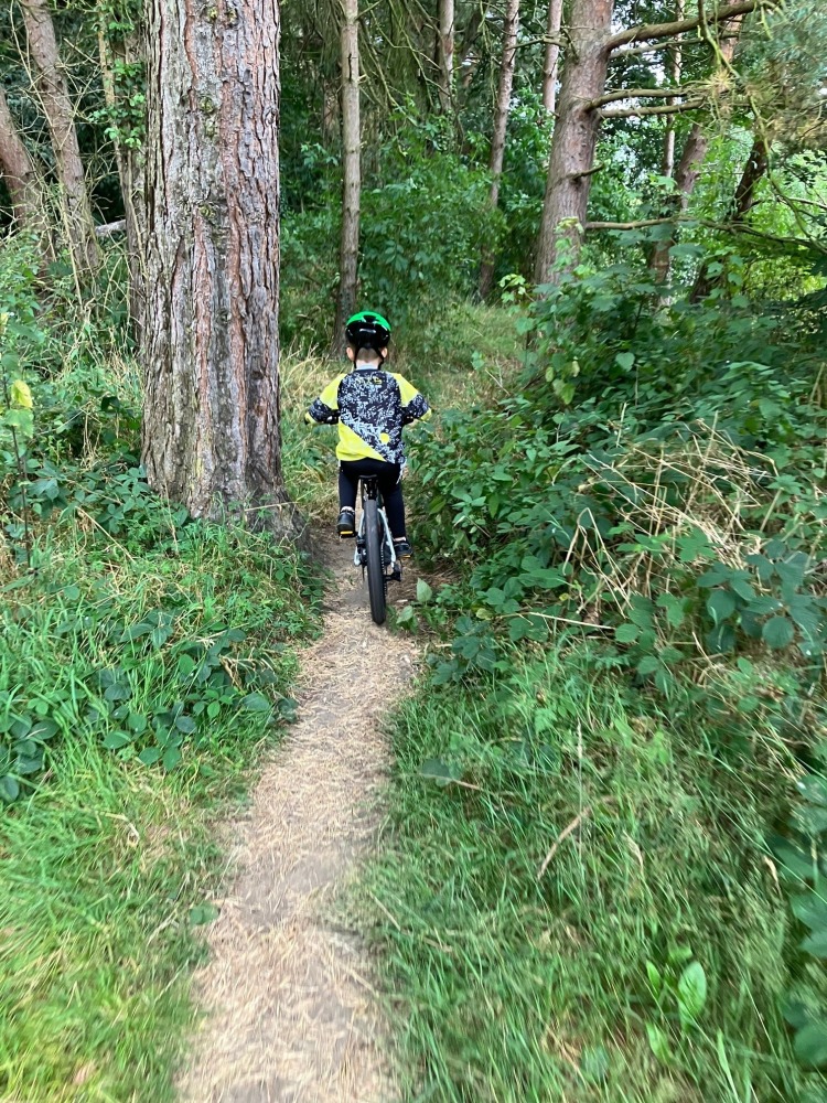 woom OFF 4 review, a photo of Zack, the reviewer in a yellow tshirt riding the black woom off 4 on a narrow trail between trees