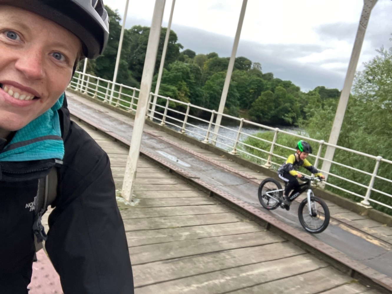 woom OFF 4 review, a photo of Zack, the reviewer in a yellow tshirt riding the black woom off 4 on a bridge with his mum