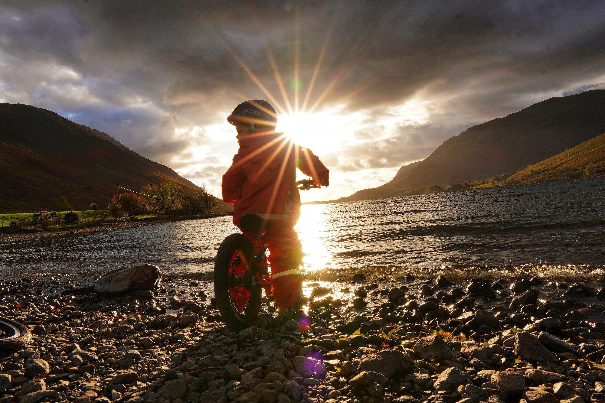 a girl in a blue coat happily gliding on her kidvelo rookie 14 balance bike by the seaside