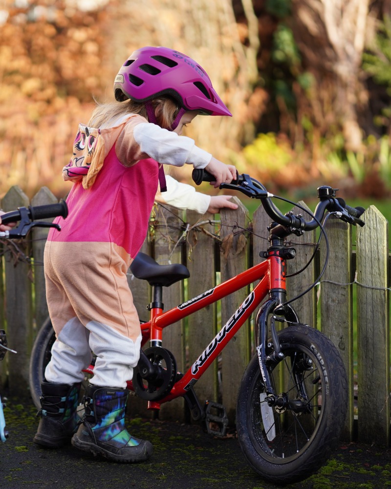 a girl in a pink oneside and pink helmet is riding the kidvelo rookie 14 to review it