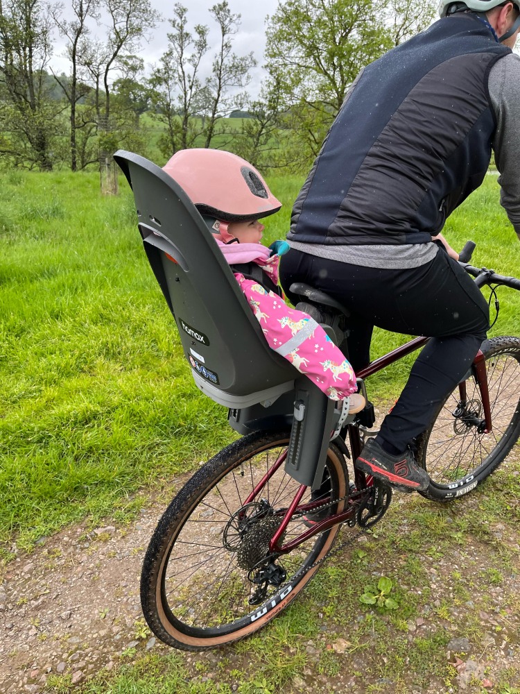 a little girl in a pink helmet in her Hamax Zenith Relax rear seat on her dads bike