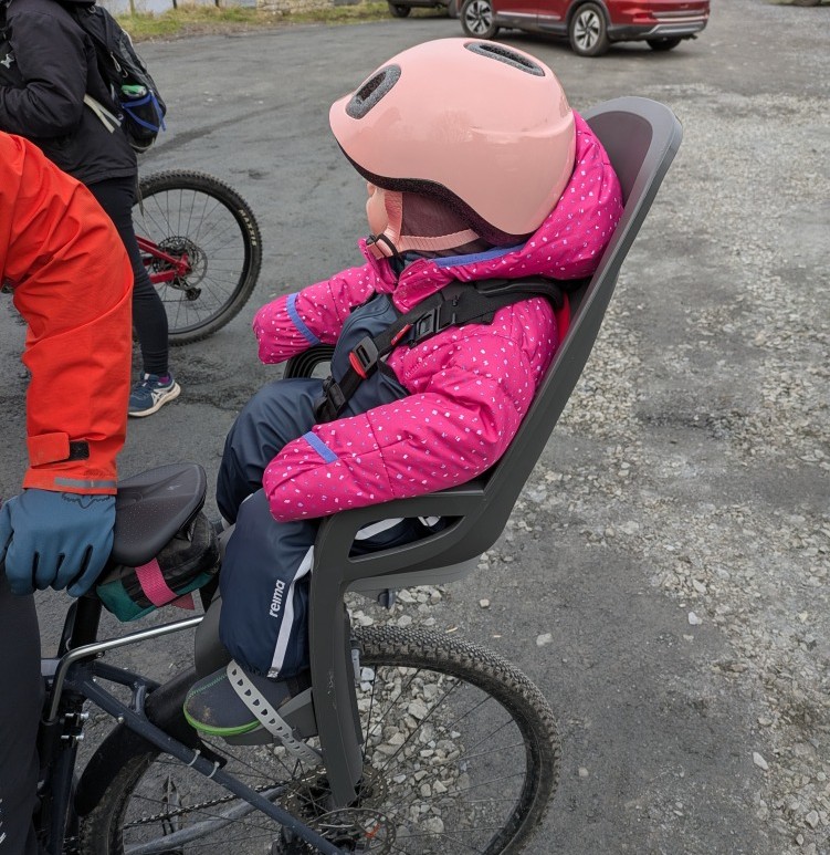 Hamax Zenith Relax Review: a little girl in a pink helmet in her Hamax Zenith Relax rear seat on her mums bike