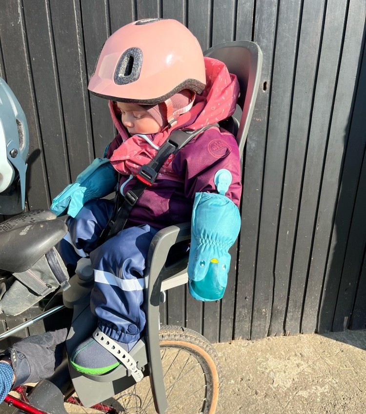 a little girl in a pink helmet in her Hamax Zenith Relax rear seat on her mums bike