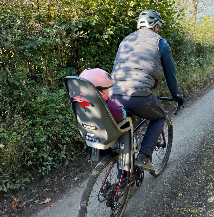 Hamax Zenith Relax Review: a little girl in a pink helmet in her Hamax Zenith Relax rear seat on her dads bike